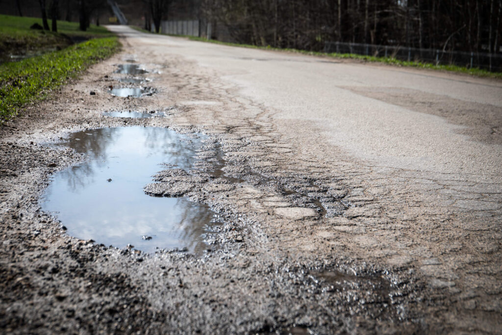 Puddles and damaged asphalt road edge. Sunny day.