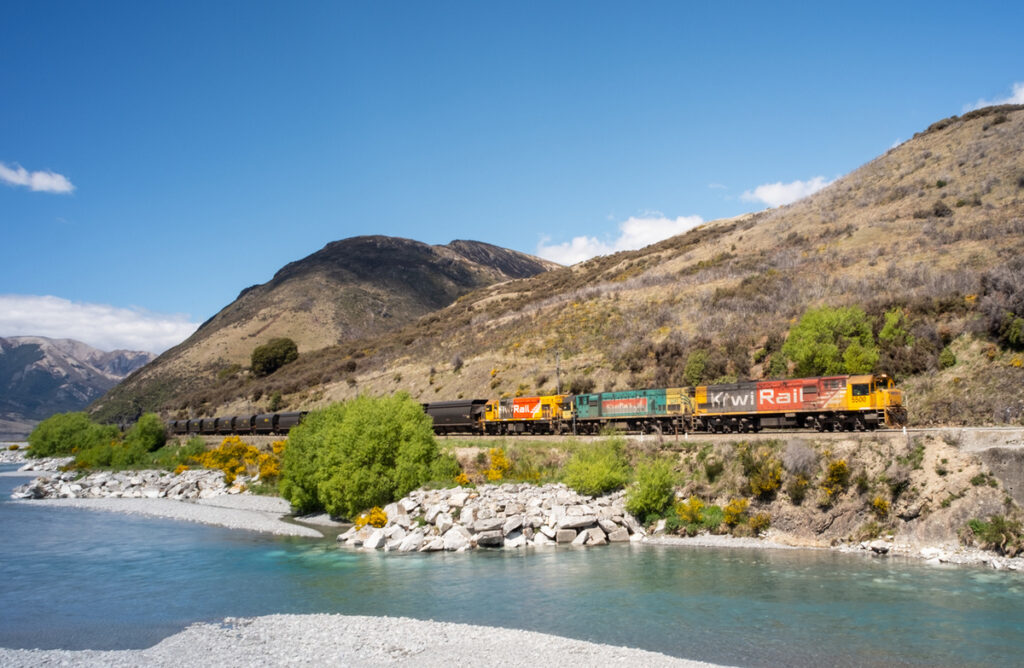 A KiwiRail freight train travels by the water and mountains in New Zealand